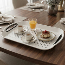 تحميل الصورة في عارض المعرض، A white rectangular serving tray with black handles and a perforated dot pattern, styled on a wooden dining table with two cups of coffee, a glass of orange juice, and a small dessert.
