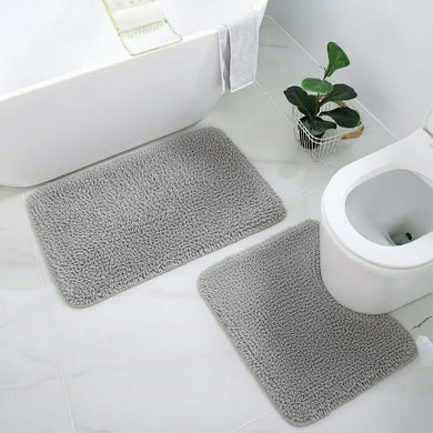 Gray bath mats on a bathroom floor with a toilet and plant in the background.