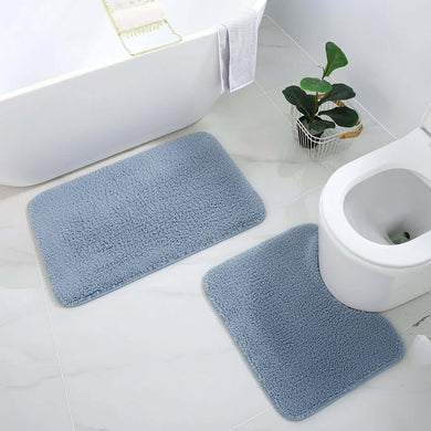 Two blue bath mats on a bathroom floor with a toilet and plant in the background.