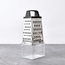 Load image into Gallery viewer, A stainless steel box grater with a clear plastic collection container underneath, shown on a gray surface against a white background.
