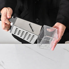 Load image into Gallery viewer, A stainless steel multi-function vegetable slicer and dicer held by a person wearing a black coat, next to a clear acrylic measuring container with measurement markings, over a white marble countertop.
