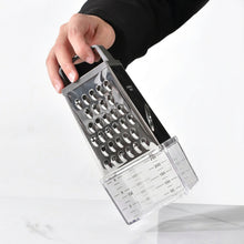 Load image into Gallery viewer, A hand holding a stainless steel box grater with a clear plastic measuring container attached, shown against a white marble-like surface and black clothing background. The YIGYI brand logo is visible in the top left.
