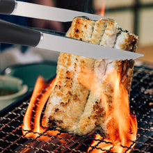 Load image into Gallery viewer, Grilled fish being cut with tongs over a flame on a grill
