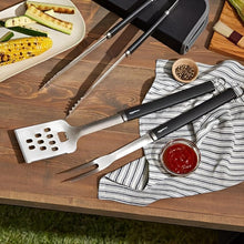 Load image into Gallery viewer, Barbecue utensils on a wooden table with grilled vegetables and a small bowl of sauce.
