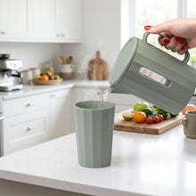 Load image into Gallery viewer, Green kettle pouring water into a green cup on a white surface with a blurred background.
