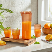 Load image into Gallery viewer, Set of orange glasses and a carafe on a wooden tray with fruits and a plant in the background.
