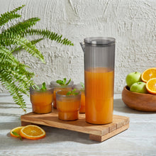 Load image into Gallery viewer, Orange juice in a carafe with glasses on a wooden tray, surrounded by fruits and a plant.
