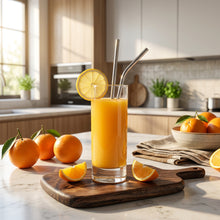 تحميل الصورة في عارض المعرض، Orange juice in a glass with lemon slice and straws on a wooden tray, surrounded by oranges and ice cubes.
