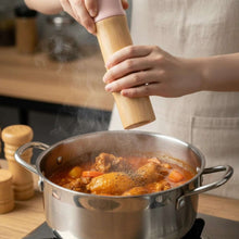 تحميل الصورة في عارض المعرض، Person seasoning a pot of stew with a wooden pepper grinder in a kitchen setting.
