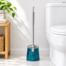 تحميل الصورة في عارض المعرض، A toilet brush with a light gray handle and a translucent teal blue base, resting on a blue and gold patterned cushion in a home setting.
