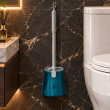 تحميل الصورة في عارض المعرض، A toilet brush with a gray handle and a translucent teal stand, placed on a tiled bathroom floor next to a white toilet.
