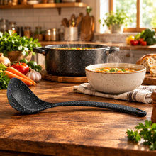 تحميل الصورة في عارض المعرض، Black ladle on a wooden kitchen counter with a blurred background of a kitchen.
