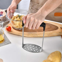 تحميل الصورة في عارض المعرض، Person using a metal potato masher on a wooden cutting board with a glass bowl of mashed potatoes.
