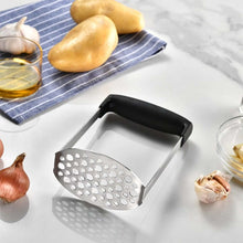 تحميل الصورة في عارض المعرض، Metal potato masher on a kitchen counter with potatoes and garlic in the background.
