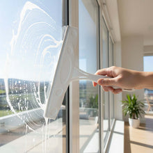 Load image into Gallery viewer, Person cleaning a glass window with a squeegee in a bright room.
