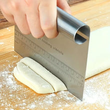 Load image into Gallery viewer, Hand using a metal bench scraper to cut dough on a wooden surface.
