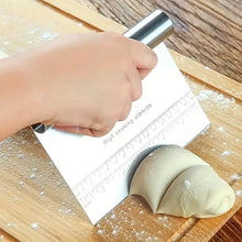 Load image into Gallery viewer, A hand holds a metal dough scraper with a built-in measuring ruler over a wooden cutting board, using it to divide dough into two pieces.
