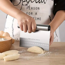 Load image into Gallery viewer, A stainless steel pastry scraper with a ruler and stencil guide, being used by a person to cut dough on a wooden table with flour.
