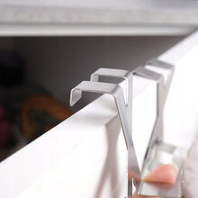 Load image into Gallery viewer, Close-up of a silver metal cabinet organizer hook mounted on the front edge of a white drawer, with a hand holding a matching hook in the foreground.
