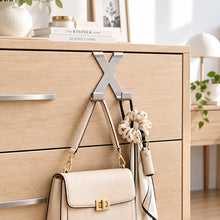 Load image into Gallery viewer, A metal wall-mounted organizer rack with two hanging loops attached to a light wood cabinet door. A pink plush toy and a red handheld device hang from the loops, with a keyboard visible on a shelf in the background.
