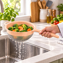 تحميل الصورة في عارض المعرض، A small kitchen strainer with a peach-colored plastic frame and handle, and a gray metal mesh bottom, shown on a plain white background.
