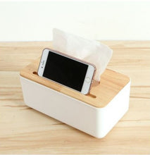 تحميل الصورة في عارض المعرض، A white plastic tissue box holder with a wooden cover, positioned on a wooden surface, with a mobile phone resting on top of the tissue box.
