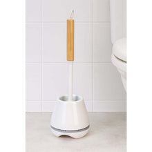 Load image into Gallery viewer, White toilet brush with wooden handle in a holder against a bathroom wall.
