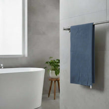 Load image into Gallery viewer, Blue towel hanging on a towel rack in a bathroom with a white bathtub and gray walls.
