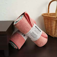 Load image into Gallery viewer, Pink rolled-up yoga mat with a label on a wooden surface next to a wicker basket.
