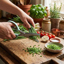 Load image into Gallery viewer, A close-up of a hand using a pair of kitchen shears with mint green handles to chop green onions on a white background.
