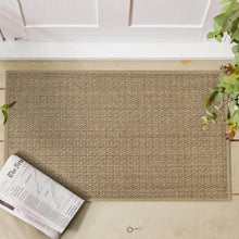 تحميل الصورة في عارض المعرض، Textured doormat on a wooden floor with a newspaper and key on it, plants on either side.

