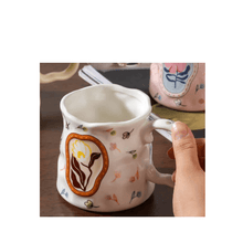 Load image into Gallery viewer, Colorful floral porcelain mug held in hand, featuring delicate butterfly and flower designs.

