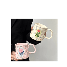 Load image into Gallery viewer, Two colorful porcelain mugs with floral designs, held in hand against a neutral background.
