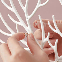 Load image into Gallery viewer, Hands organizing jewelry on a white deer-shaped stand, showcasing earrings and necklaces in a stylish manner.
