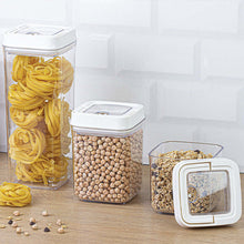 Load image into Gallery viewer, Three transparent storage containers with white lids, filled with pasta, beans, and cereal, on a wooden surface.
