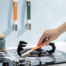 Load image into Gallery viewer, A hand is using an orange kitchen gas stove cleaning brush with plastic scraper on a black gas stove top.
