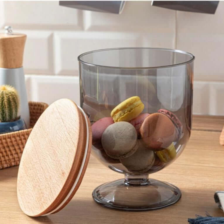 A transparent acrylic food storage container with a wooden lid, filled with various cookies and placed on a table.